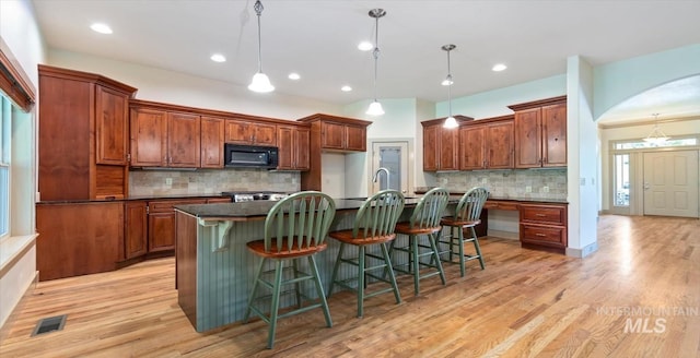 1563 W Colville Ct, Eagle, ID 83616 - kitchen with black microwave, dark countertops, backsplash, an island with sink, and light wood-style floors