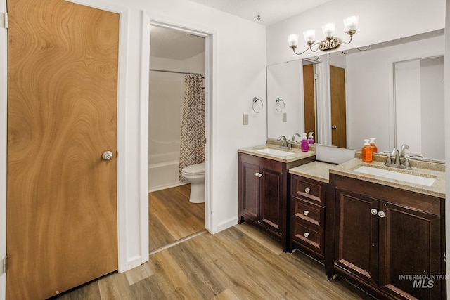 full bath with a sink, an inviting chandelier, double vanity, and wood finished floors