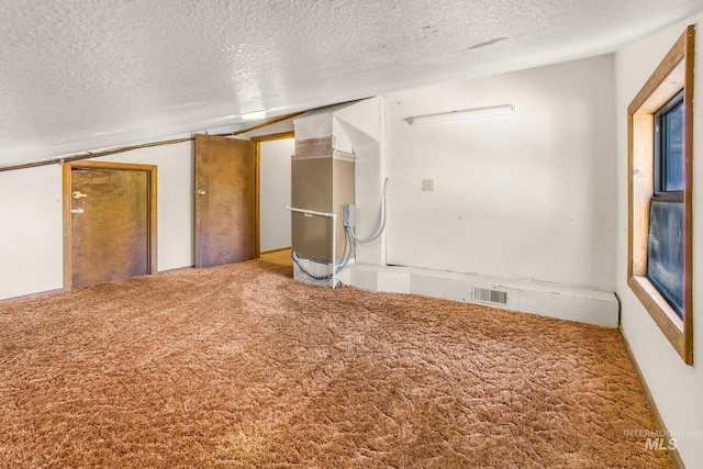 empty room featuring a textured ceiling, visible vents, vaulted ceiling, and carpet