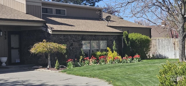 view of property exterior with fence, a shingled roof, a yard, and stone siding