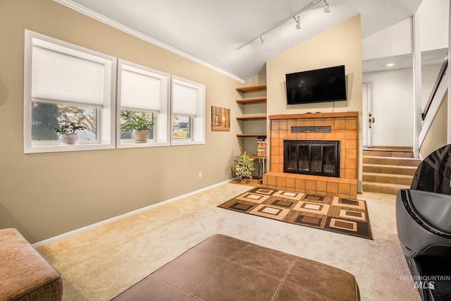 carpeted living room featuring crown molding, a fireplace, vaulted ceiling, track lighting, and stairs