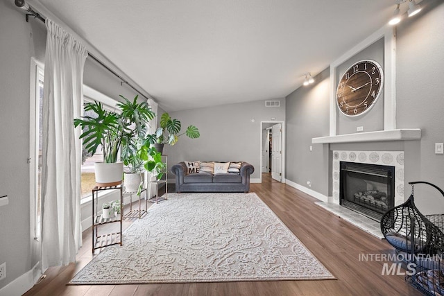 living area featuring visible vents, vaulted ceiling, wood finished floors, a tile fireplace, and baseboards