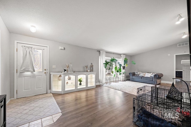 living area with visible vents, vaulted ceiling, a textured ceiling, wood finished floors, and baseboards