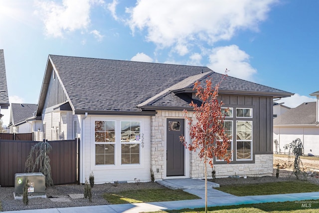 view of front facade with stone siding, board and batten siding, fence, and roof with shingles