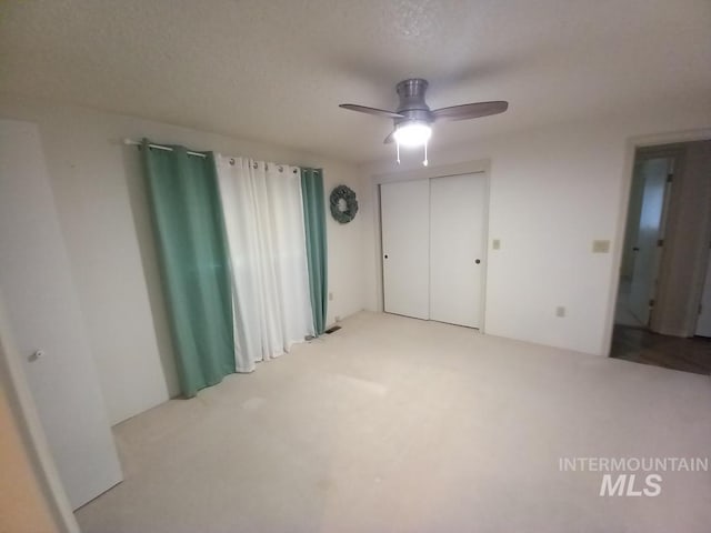 unfurnished bedroom with ceiling fan, light colored carpet, a textured ceiling, and a closet