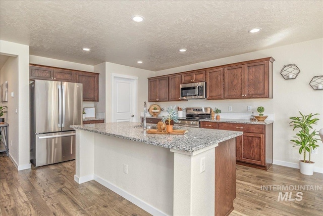 19118 Ralston Way, Caldwell, ID 83605 - kitchen featuring stainless steel appliances, wood finished floors, light stone counters, an island with sink, and a textured ceiling