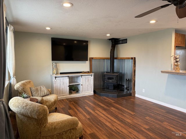 living room with baseboards, ceiling fan, recessed lighting, a wood stove, and wood finished floors