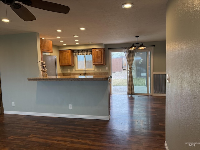 kitchen featuring dark wood-type flooring, a ceiling fan, freestanding refrigerator, brown cabinetry, and baseboards