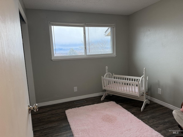 unfurnished bedroom featuring visible vents, baseboards, a textured ceiling, and dark wood finished floors