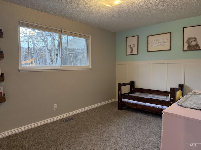 bedroom with visible vents, a wainscoted wall, a textured ceiling, carpet flooring, and a decorative wall