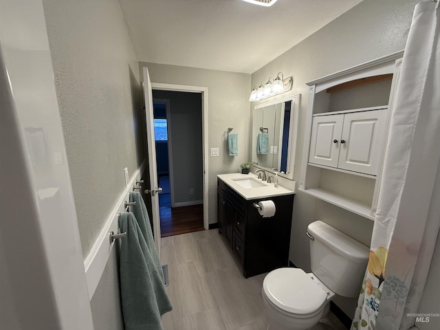 bathroom with vanity, wood finished floors, visible vents, toilet, and a textured wall