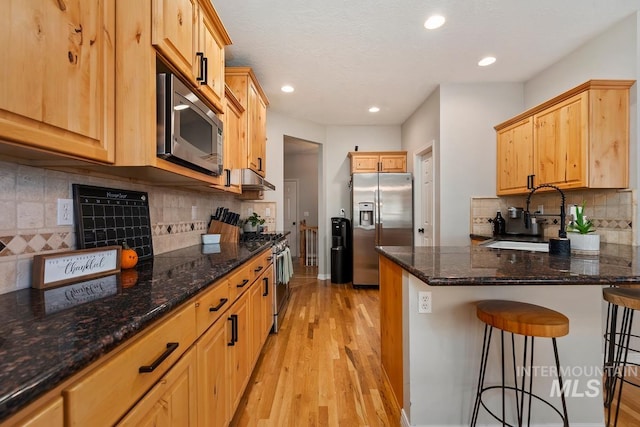 kitchen featuring a breakfast bar, light hardwood / wood-style flooring, dark stone countertops, appliances with stainless steel finishes, and tasteful backsplash