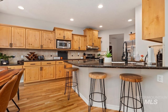 kitchen featuring dark stone counters, a breakfast bar, light hardwood / wood-style flooring, and stainless steel appliances