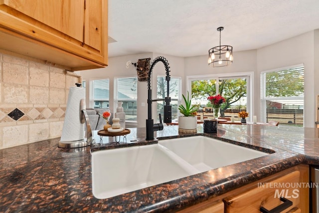 kitchen with a textured ceiling, sink, an inviting chandelier, dark stone countertops, and hanging light fixtures