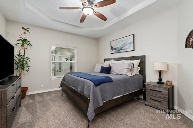 carpeted bedroom featuring ceiling fan and a raised ceiling