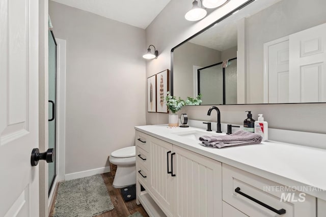 bathroom featuring wood-type flooring, vanity, toilet, and a shower with shower door