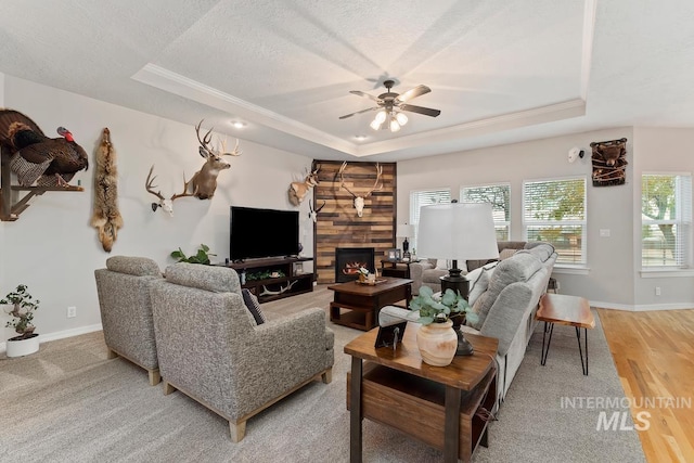 living room with hardwood / wood-style floors, a raised ceiling, ceiling fan, a textured ceiling, and a large fireplace