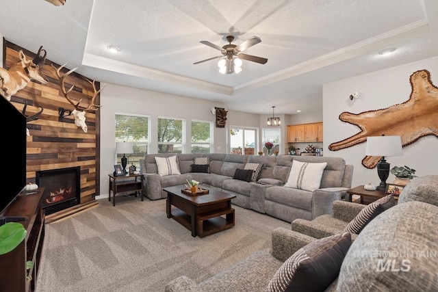 carpeted living room featuring a textured ceiling, a tray ceiling, ceiling fan, wooden walls, and a stone fireplace