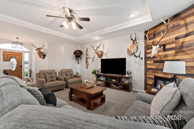 living room with ornamental molding, a tray ceiling, ceiling fan, carpet floors, and wood walls