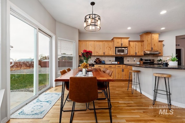 kitchen with an inviting chandelier, hanging light fixtures, decorative backsplash, light wood-type flooring, and appliances with stainless steel finishes