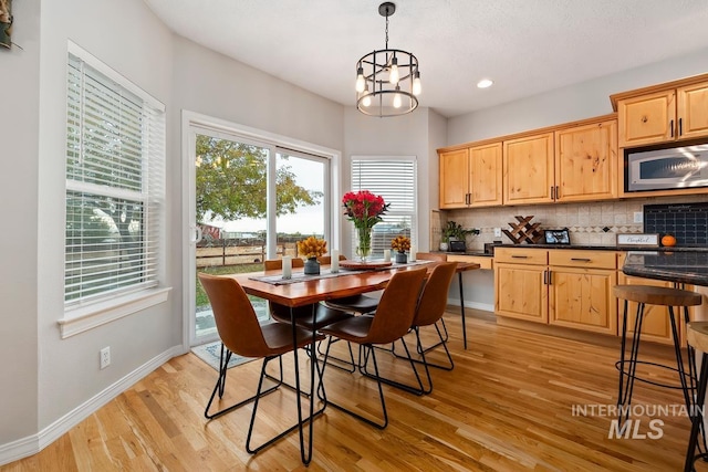 kitchen featuring stainless steel microwave, backsplash, an inviting chandelier, light wood-type flooring, and decorative light fixtures