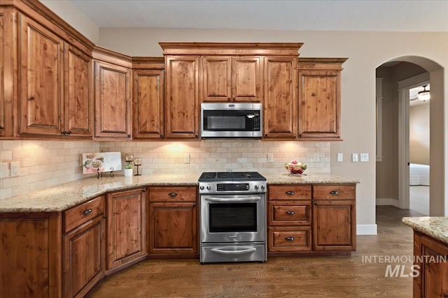 kitchen with brown cabinets, light stone countertops, arched walkways, and stainless steel appliances