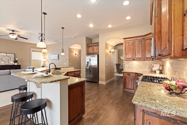kitchen with brown cabinetry, arched walkways, stainless steel fridge with ice dispenser, and a sink