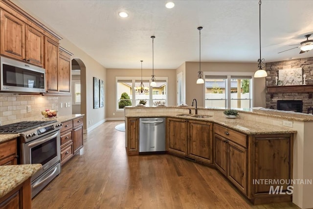 kitchen with a stone fireplace, a sink, stainless steel appliances, brown cabinets, and backsplash