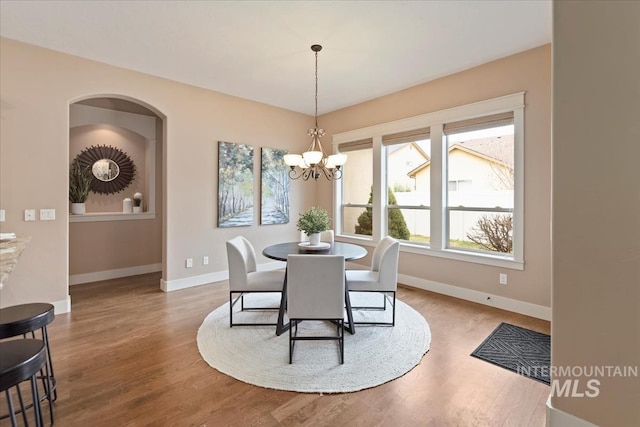 dining space featuring a chandelier, arched walkways, wood finished floors, and baseboards