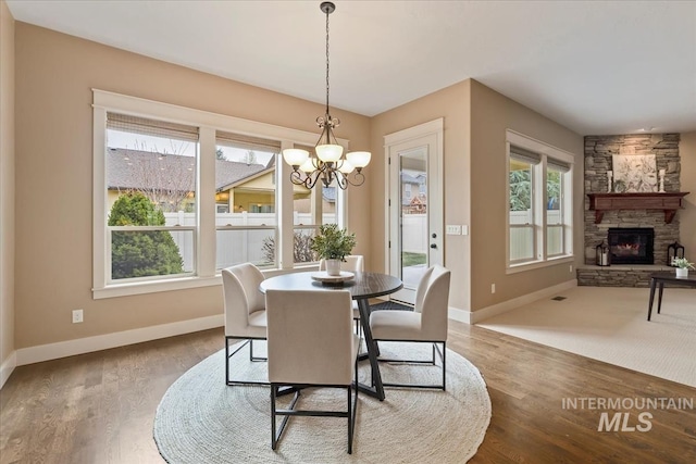 dining area featuring wood finished floors, an inviting chandelier, baseboards, and a fireplace