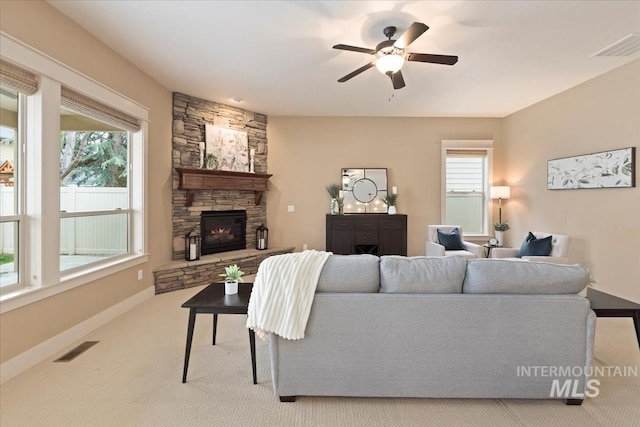 living area with a stone fireplace, baseboards, visible vents, ceiling fan, and carpet