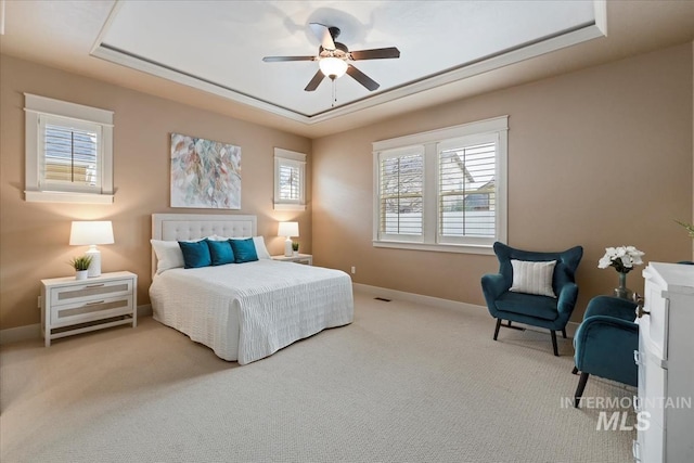 carpeted bedroom with a tray ceiling, baseboards, and a ceiling fan
