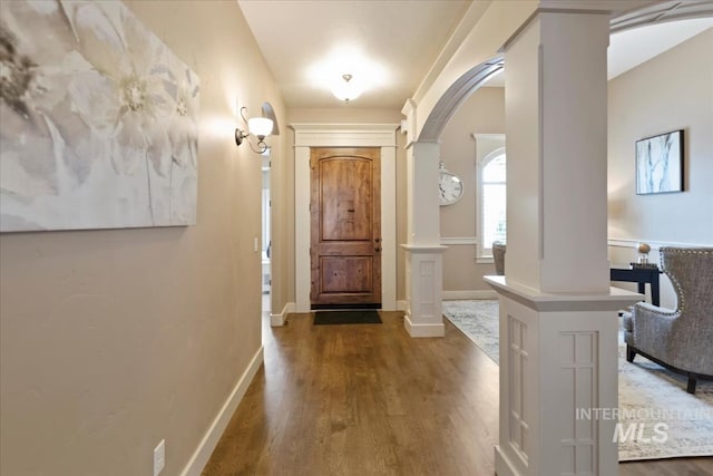 entryway featuring arched walkways, ornate columns, baseboards, and wood finished floors