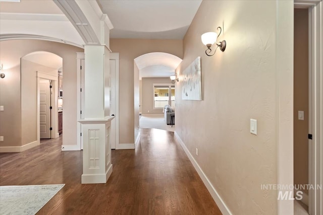 corridor featuring arched walkways, dark wood-type flooring, and baseboards
