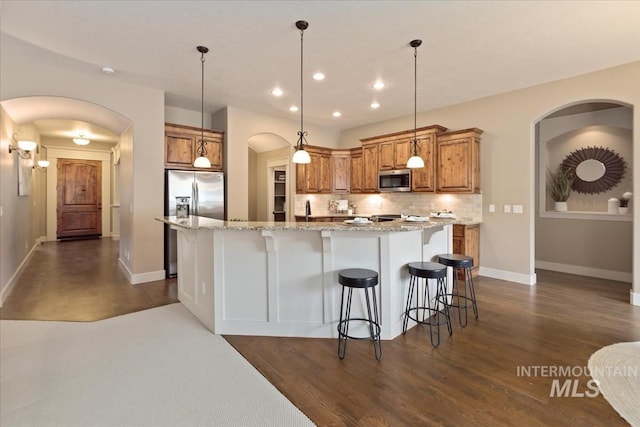kitchen featuring arched walkways, appliances with stainless steel finishes, dark wood-style floors, brown cabinets, and backsplash