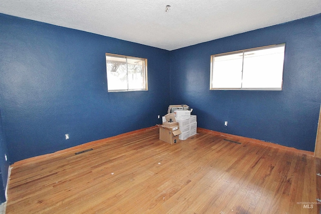 unfurnished room with a textured ceiling, wood-type flooring, visible vents, and baseboards