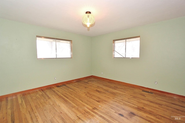 spare room with light wood-type flooring, a healthy amount of sunlight, visible vents, and baseboards