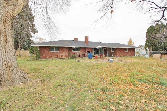 rear view of property with brick siding, a chimney, fence, and a yard