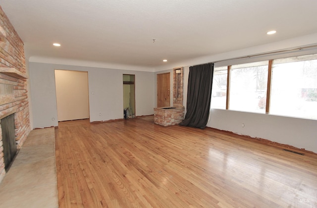 unfurnished living room featuring light wood finished floors, a stone fireplace, visible vents, and recessed lighting