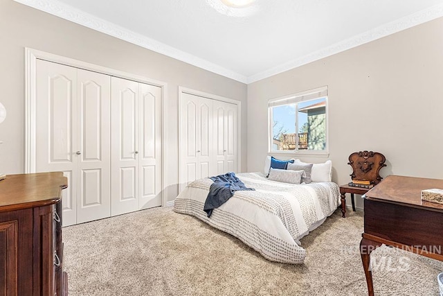 bedroom with two closets, crown molding, and carpet flooring