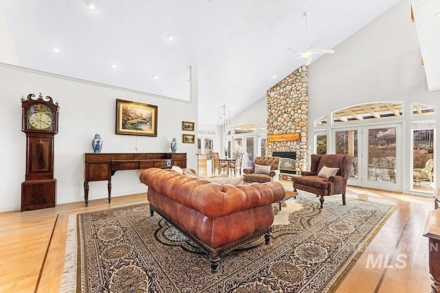 living room featuring high vaulted ceiling, light wood-type flooring, ceiling fan, and a stone fireplace