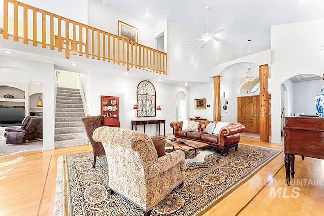 living room with a high ceiling, ceiling fan, light wood-type flooring, and built in features