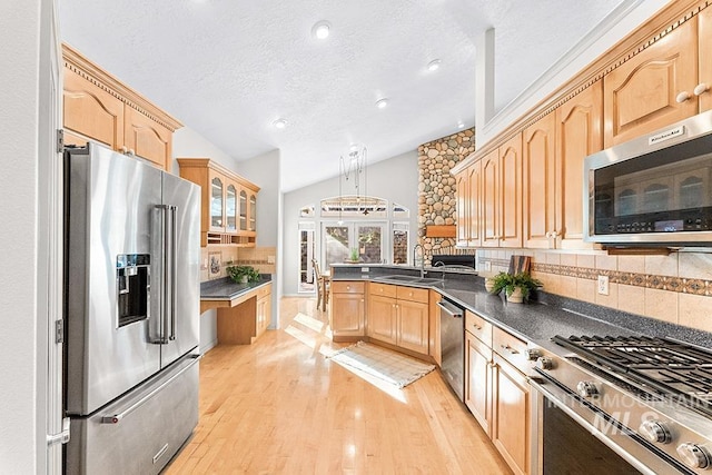 kitchen with vaulted ceiling, stainless steel appliances, light wood-type flooring, light brown cabinets, and backsplash