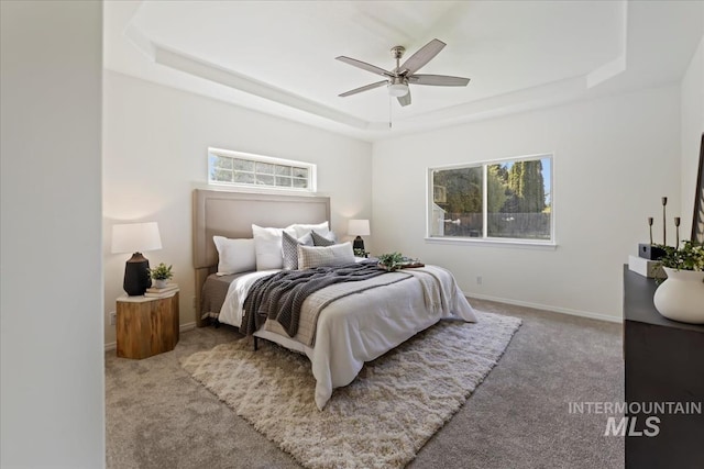 carpeted bedroom with a tray ceiling, multiple windows, baseboards, and ceiling fan
