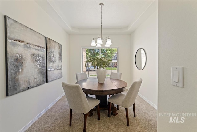 carpeted dining area with a chandelier, a tray ceiling, and baseboards