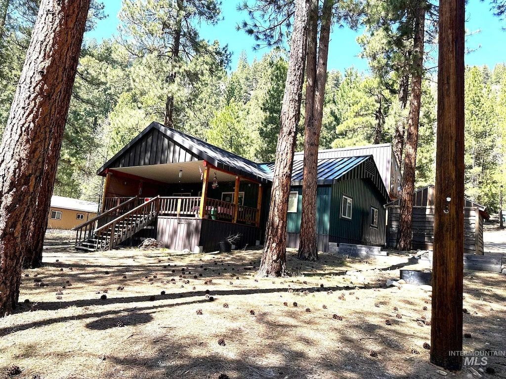 view of front of house with board and batten siding, a porch, stairway, metal roof, and a wooded view