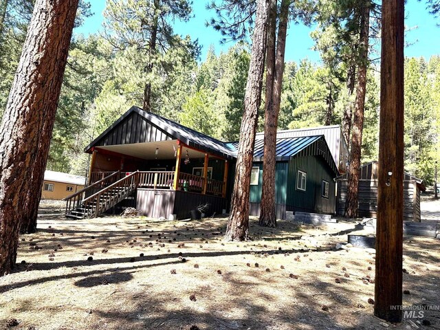 view of front of house with board and batten siding, a porch, stairway, metal roof, and a wooded view