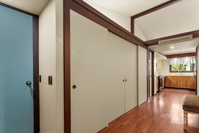hall with a sink, light wood-style floors, and vaulted ceiling