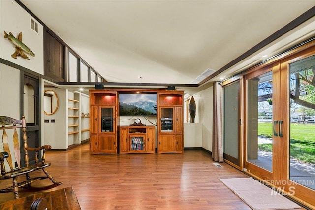 unfurnished living room with built in features, baseboards, wood finished floors, and visible vents