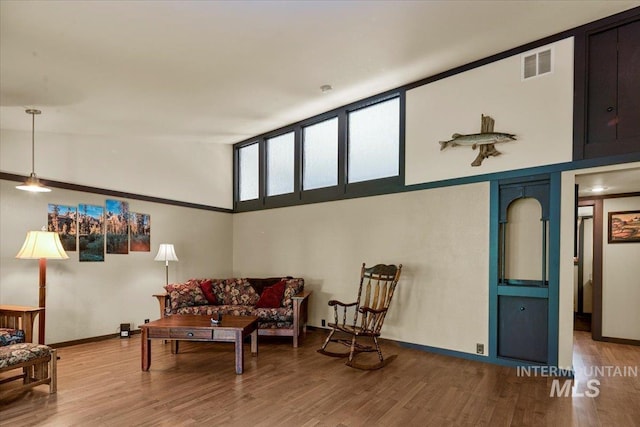 living area with baseboards, a high ceiling, visible vents, and wood finished floors